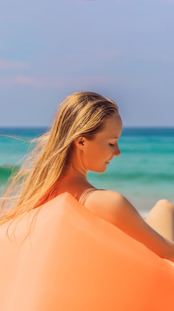 Summer lifestyle portrait of pretty girl sitting on the orange inflatable sofa on the beach of