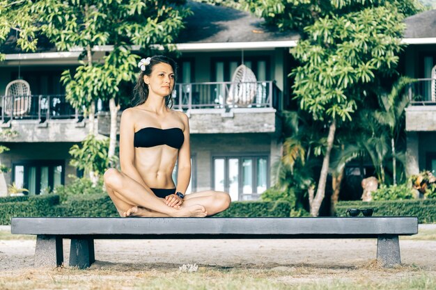 Photo summer lifestyle portrait of pretty happy young girl sitting on bench at the tropical island beach