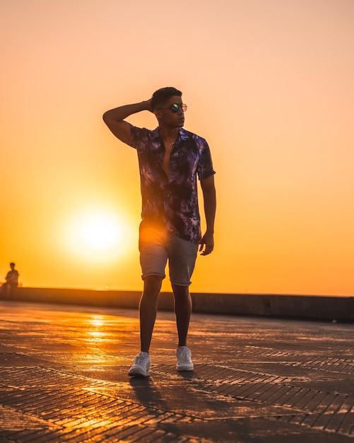 夏のライフスタイル紫色の花のシャツとサングラスが夕日を散歩して夏休みを楽しんでいる若いラテン系アメリカ人