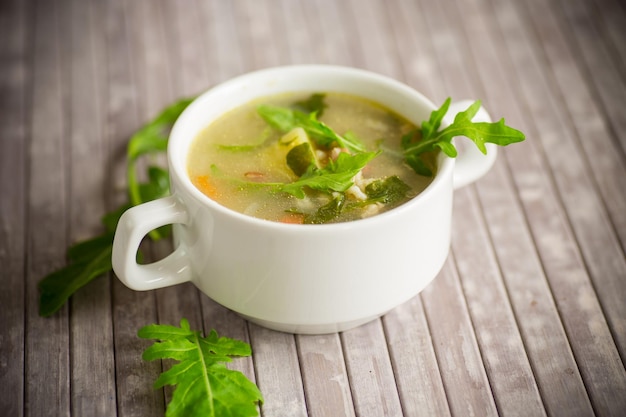 Summer light soup with oatmeal and arugula in a plate on the table