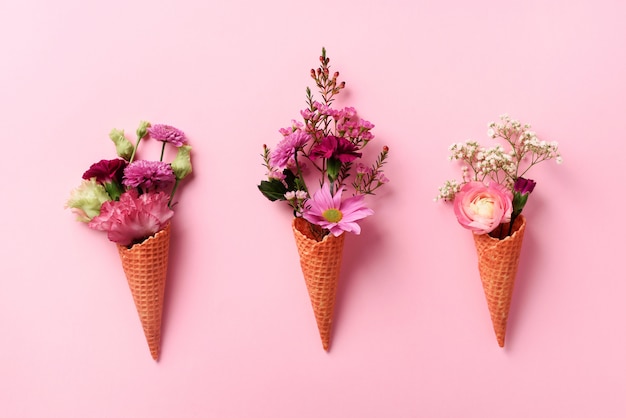 Summer minimal concept. Ice cream cone with pink flowers and leaves on punchy pastel background. 