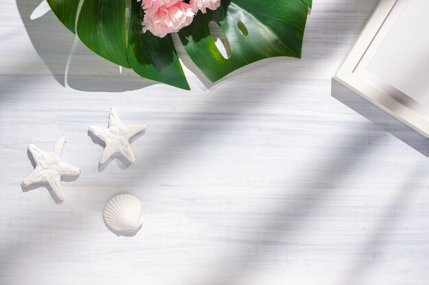  summer monstera and shell and starfish on white wood table with sunlight shadow.