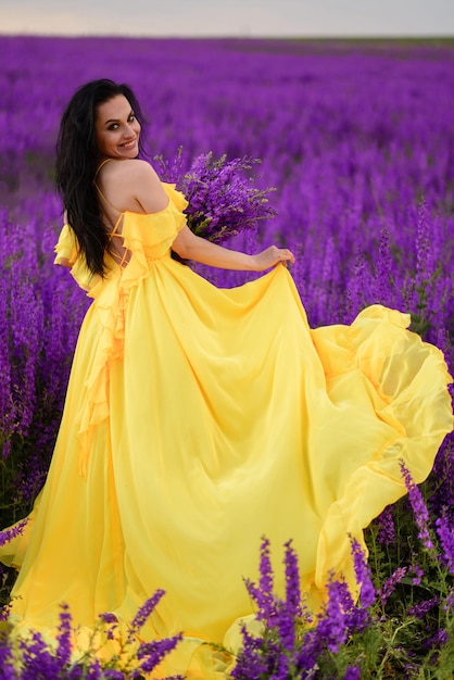 Photo summer mood. a woman in a luxurious yellow dress walks along a purple blooming field with her back to the camera.