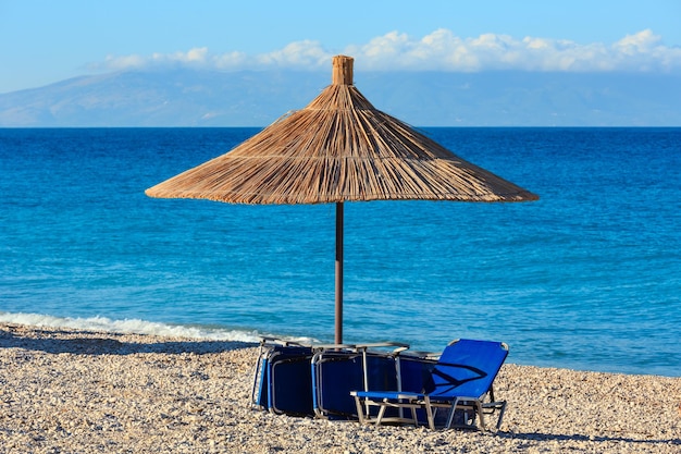 Summer morning pebbly beach with sunbeds and strawy sunshades (Borsh, Albania).