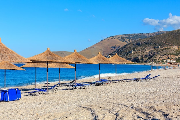 Summer morning pebbly beach with sunbeds and strawy sunshades (Borsh, Albania).