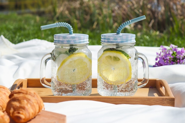 Summer outdoor picnic with two jars of fresh lemonade and croissants