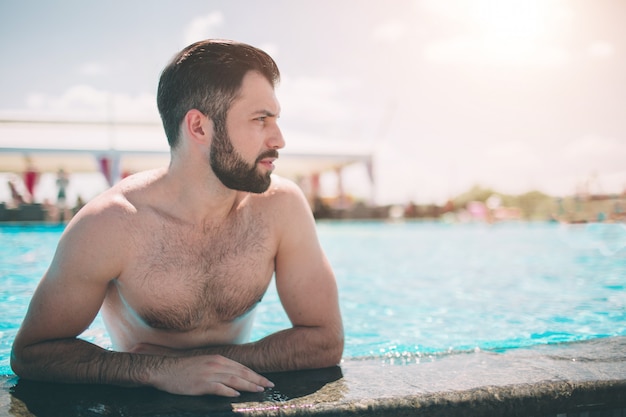 Summer photo of muscular smiling man in swimming pool. Happy male model in water on summer vacations.