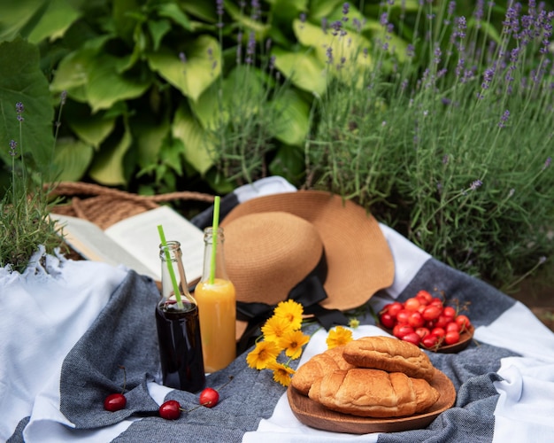 Picnic estivo nel campo di lavanda. natura morta picnic estivo all'aperto con frutti di bosco, cappello di paglia e succo di frutta