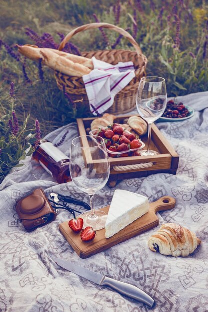 Foto estate - picnic nel prato. brie al formaggio, baguette, fragola, ciliegia, vino, croissant e cestino