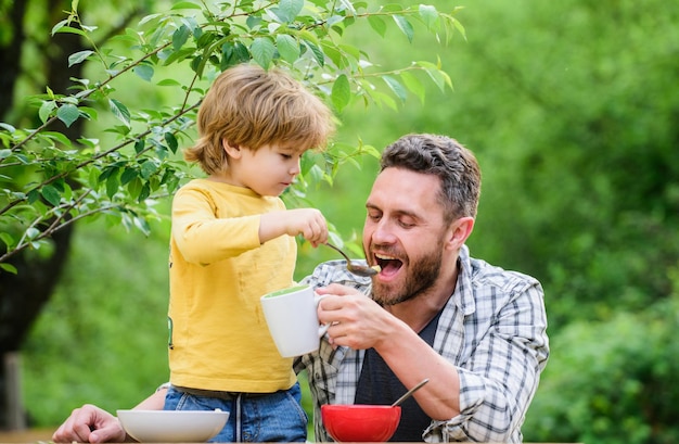 夏のピクニック朝の朝食家族の夕食の時間幸せな父親の日お父さんと一緒に小さな男の子が穀物の健康的な食べ物を食べる子供の日父と息子が屋外で食べる明るい瞬間を一緒にキャプチャする