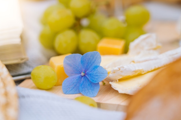 Picnic estivo in una giornata di sole con pane, frutta, bouquet di fiori di ortensie, bicchieri di vino, cappello di paglia, libro e ukulele.