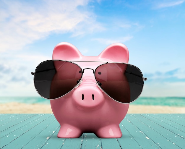 Summer piggy bank with sunglasses on the beach