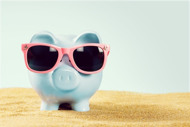 Summer piggy bank with sunglasses on the beach