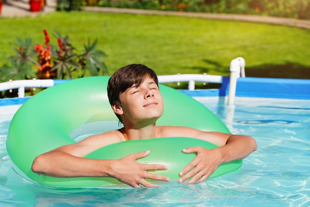 Piscina estiva con cerchio verde e ragazzo ridente che prende il sole bambini nella piscina satura di b...