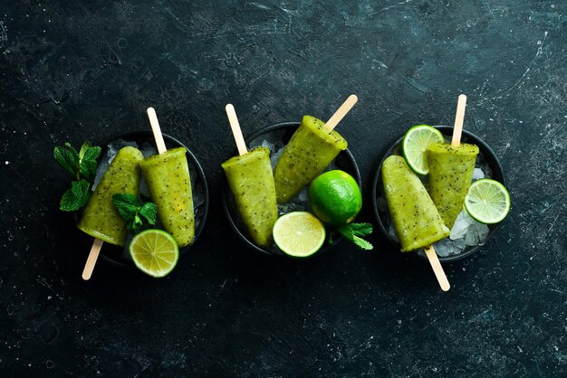 Summer popsicles with lime and kiwi On a black stone background