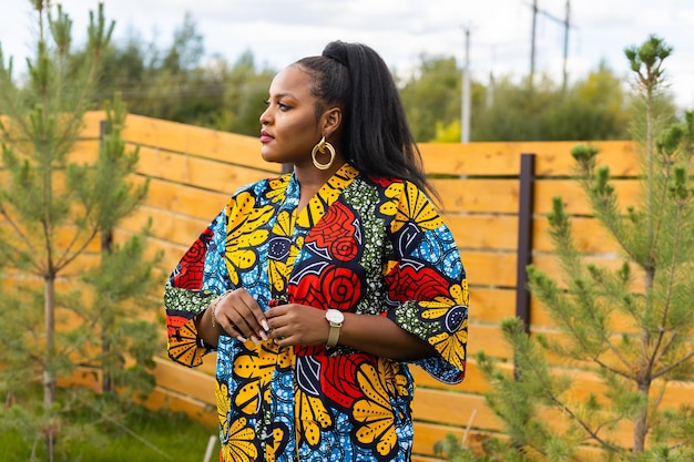 Photo summer portrait of beautiful african american woman in colourful dress wear standing on backyard suburban lifestyle and chilling on weekend in countryside and inclusion with diversity concept