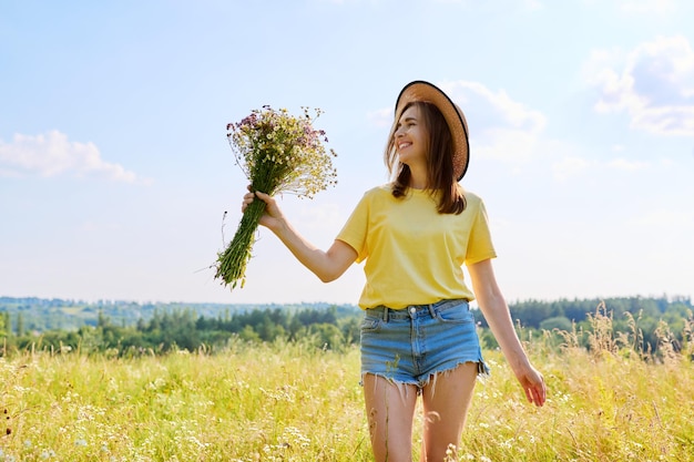 野生の花の花束を持つ幸せな女性の夏の肖像画