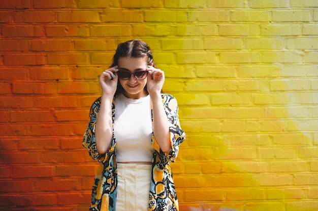 화려한 오렌지색 배경에 선글라스를 끼고 웃고 있는 행복한 젊은 여성의 여름 초상화