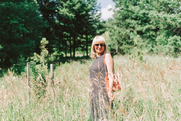 Summer portrait of mature adult blonde woman sitting in a grass on sunny day in the meadow