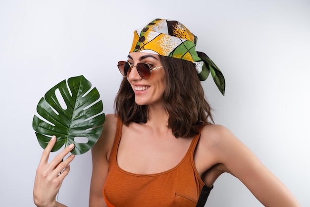 Summer portrait of a young woman in a sports swimsuit headscarf and sunglasses with monstera palm leaf