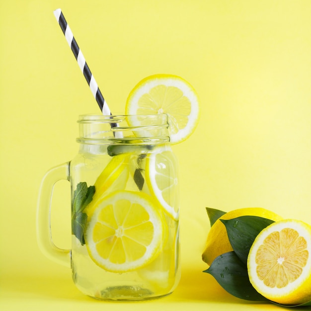 Summer refreshing cocktail with lemon, mint and ice in mason jar on yellow. Tropical concept.