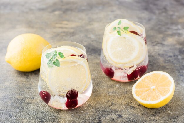 Summer refreshing cold cocktail with lemon, lemon balm and cherry - hard seltzer in glasses on the table