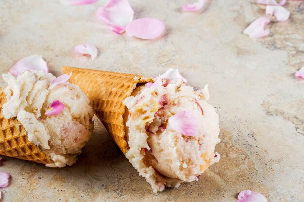 Летние освежающие десерты. Вегетарианское диетическое питание. Мороженое с лепестками роз и кусочками миндаля, в классических вафельных рожках, на бежевом светлом бетонном столе. Copyspace