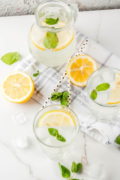 Summer refreshing drinks, mojito or lemonade with fresh mint, slices of lemon, ice, on a light surface.  top view