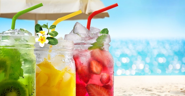 Summer refreshing exotic drinks cocktails in glass jars with straws on seascape with bokeh sun light background.