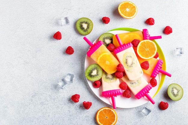 Summer refreshing homemade popsicles with oranges and kiwi Healthy snack with fruits and frozen juice for summer heat on concrete table top flat lay copy space