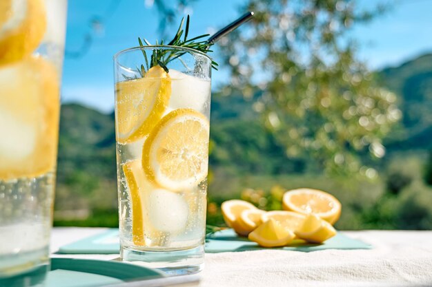 Foto l'estate bevanda rinfrescante di limonata o cocktail alcolico con rosmarino ghiacciato e fette di limone sul tavolo
