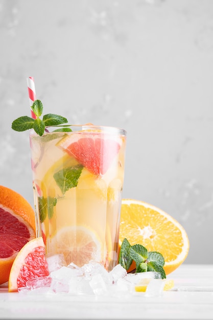 Photo summer refreshing lemonade with mint on a light background. a glass of citrus cocktail in a light key. close-up. summer vitamin cocktail of orange, lemon and grapefruit.