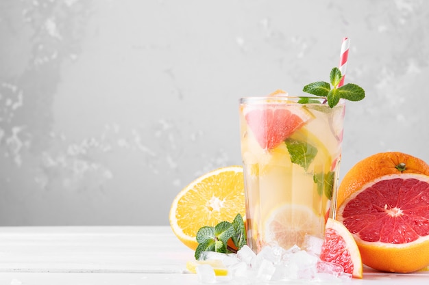 Фото Летний освежающий лимонад с мятой на светлом фоне. стакан цитрусового коктейля в светлом ключе. крупный план. летний витаминный коктейль из апельсина, лимона и грейпфрута.