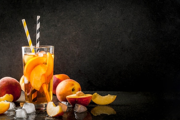 Summer refreshment drinks. Iced tea with pieces of organic homemade peach of nectarine. On a black stone background, with ice and ingredients. copyspace