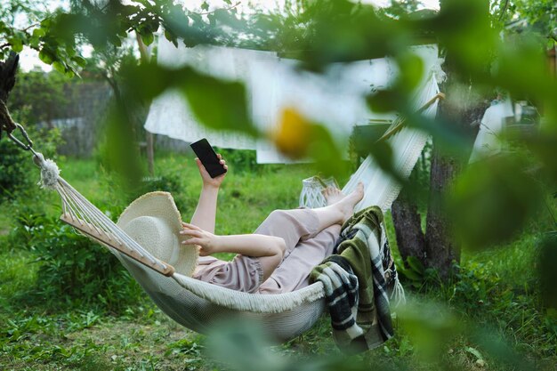 Photo summer retreat lady in a sun hat enjoys her green oasis leisurely scrolling through social media on