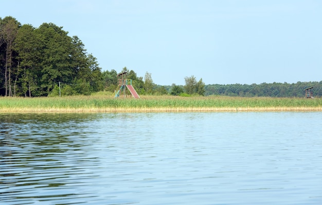 Summer rushy lake view with small grove on opposite shore and observation deck