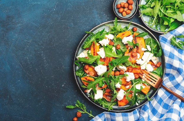 Summer salad with grilled peach with soft cheese hazelnuts and arugula on blue table background top view copy space