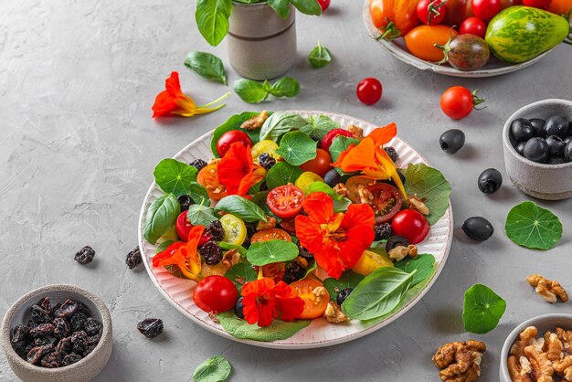 Insalata estiva con fiori di nasturzio pomodori olive uvetta e noci su sfondo grigio cibo dietetico sano