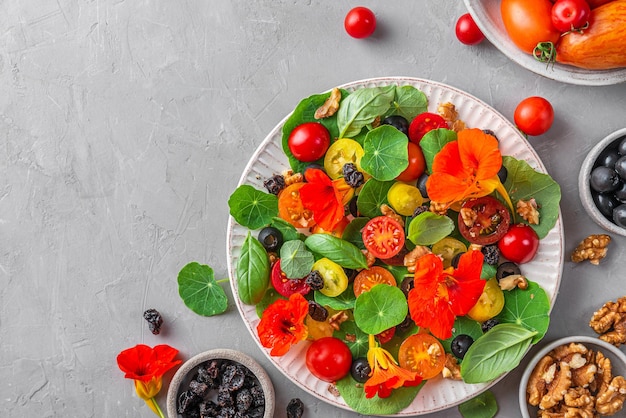 Summer salad with nasturtium flowers vegetables and nuts on gray background Healthy diet food Top view