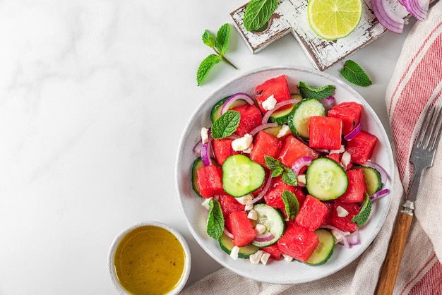 Summer salad with watermelon cucumber cheese and mint in a plate on white table Top view with copy space