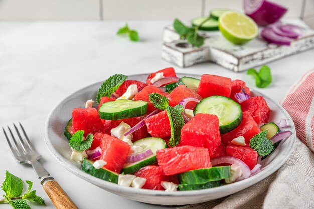 summer salad with watermelon cucumber cheese and mint in a plate on white table with fork close u