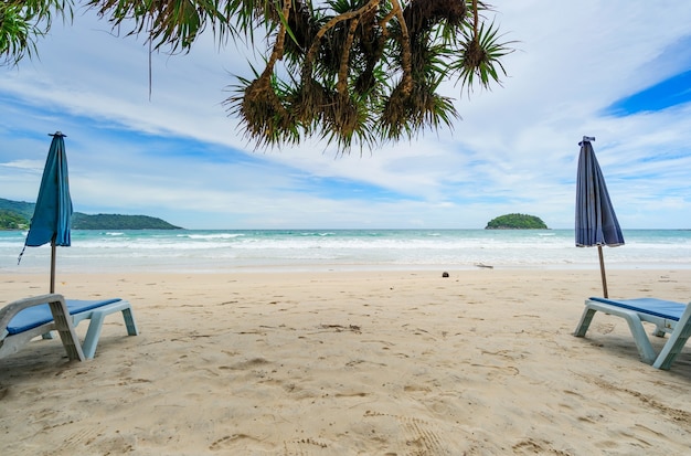 Summer sandy beach with beach chair and wave seafoam clashing on sandy shore turquoise ocean water and blue sky white clouds over sea Natural background for summer vacation Travel website.