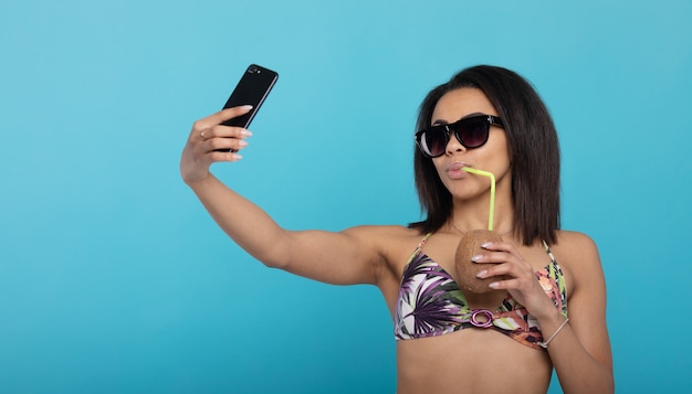 Foto selfie estivo. ragazza nera in costume da bagno che si fotografa con il cocktail fresco sul cellulare.