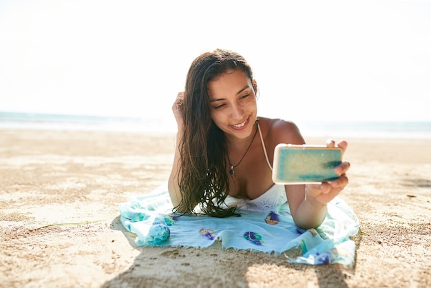 夏の自分撮りは、ビーチに横たわっている間に自分撮りをしている若い女性の最高のショットです