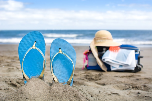 Scarpe estive sulla spiaggia di sabbia con valigia da viaggio