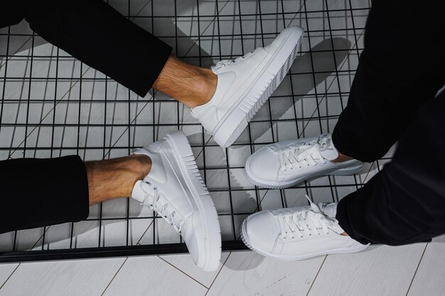 Summer shoes Closeup of male and female legs in black pants and white casual sneakers Summer leather shoes for men and women