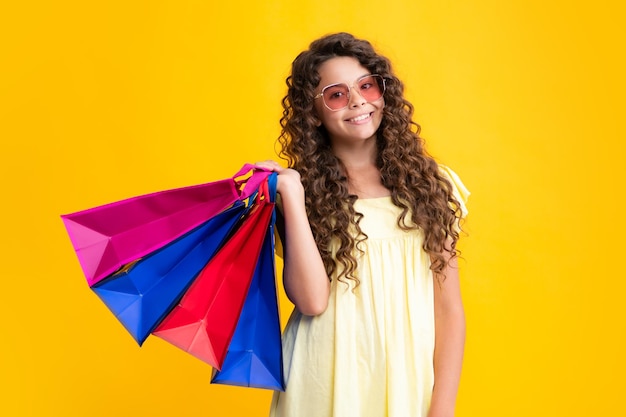 Summer shopping sale Beautiful fashion teenager child girl with shopping bags on yellow background Shopaholic shopping and fashion Kid with shopping sale bags Smiling girl