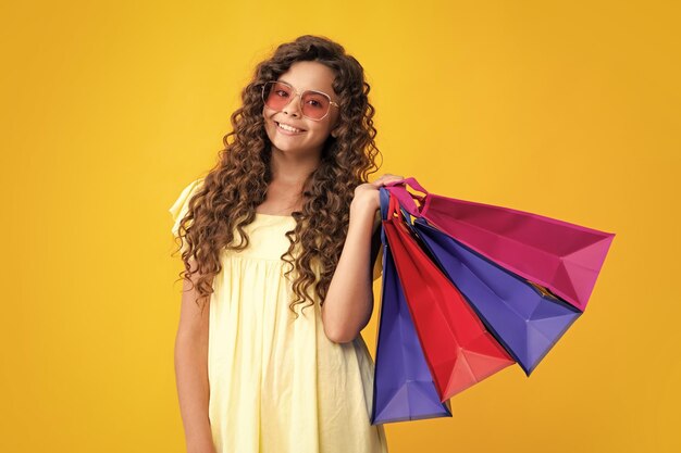 Summer shopping sale Beautiful fashion teenager child girl with shopping bags on yellow background Shopaholic shopping and fashion Kid with shopping sale bags Smiling girl