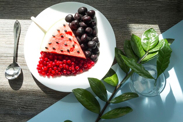 Летняя закуска Свежие ягоды и фрукты на деревянном столе с зелеными листьями растений