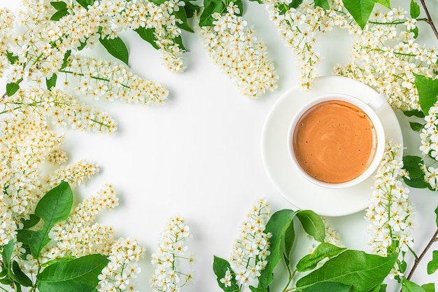 Summer-spring background with flowering branches and a cup of coffee on a white background. Top view, copy space.